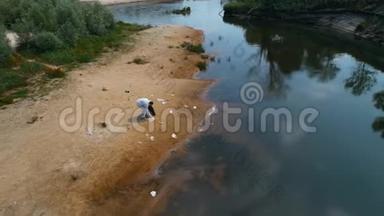 一个穿着防护服的人在干燥污染的河流岸边收集塑料垃圾的鸟瞰图